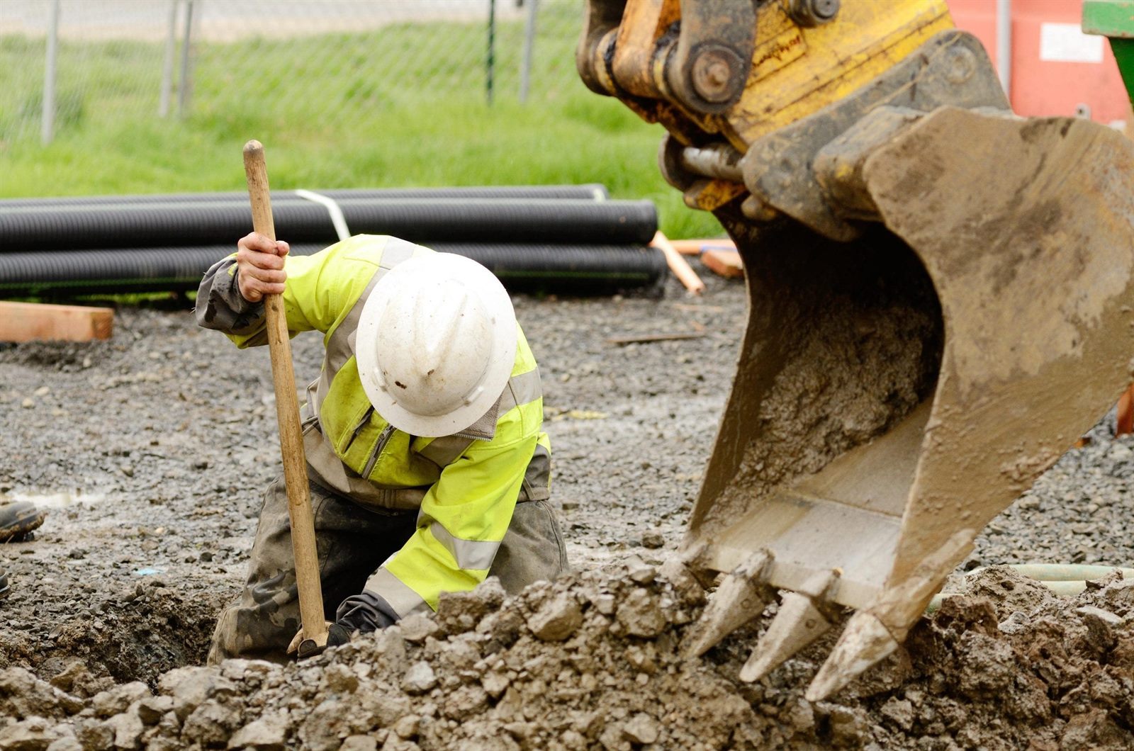 Contractor in a hard hat laying pipe beside an excavator